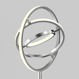 A modern floor lamp featuring three interlocking metallic rings with integrated LED lights, creating a sculptural, geometric design against a plain gray background.