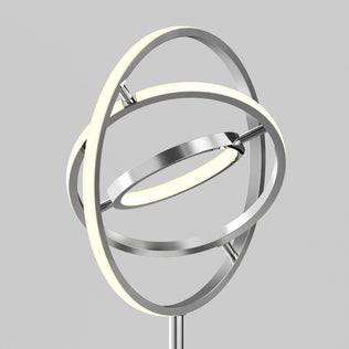The Artika Pivot modern LED floor lamp 3 CCT showcases three intersecting metallic rings with built-in LEDs, forming a geometric, sculptural design set against a plain gray background.