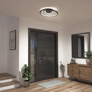 A modern entryway featuring a dark front door, Artika’s Salto LED flush mount light, a potted plant, an umbrella stand, framed wall art, and a wooden console table with a mirror and decor accents.