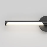 A modern wall-mounted light fixture with a black cylindrical body, emitting soft white light, attached to a round black base against a plain light gray background.