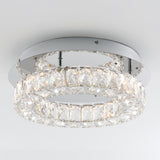 A modern flush-mount ceiling light fixture with two concentric rings adorned with clear, faceted crystals, set against a white ceiling. The light creates a sparkling effect through the crystals.