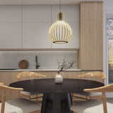 A modern kitchen with light wood cabinets, a round black dining table, four wooden chairs, a vase with branches, and a lit pendant lamp hanging above the table. A window lets in natural light.