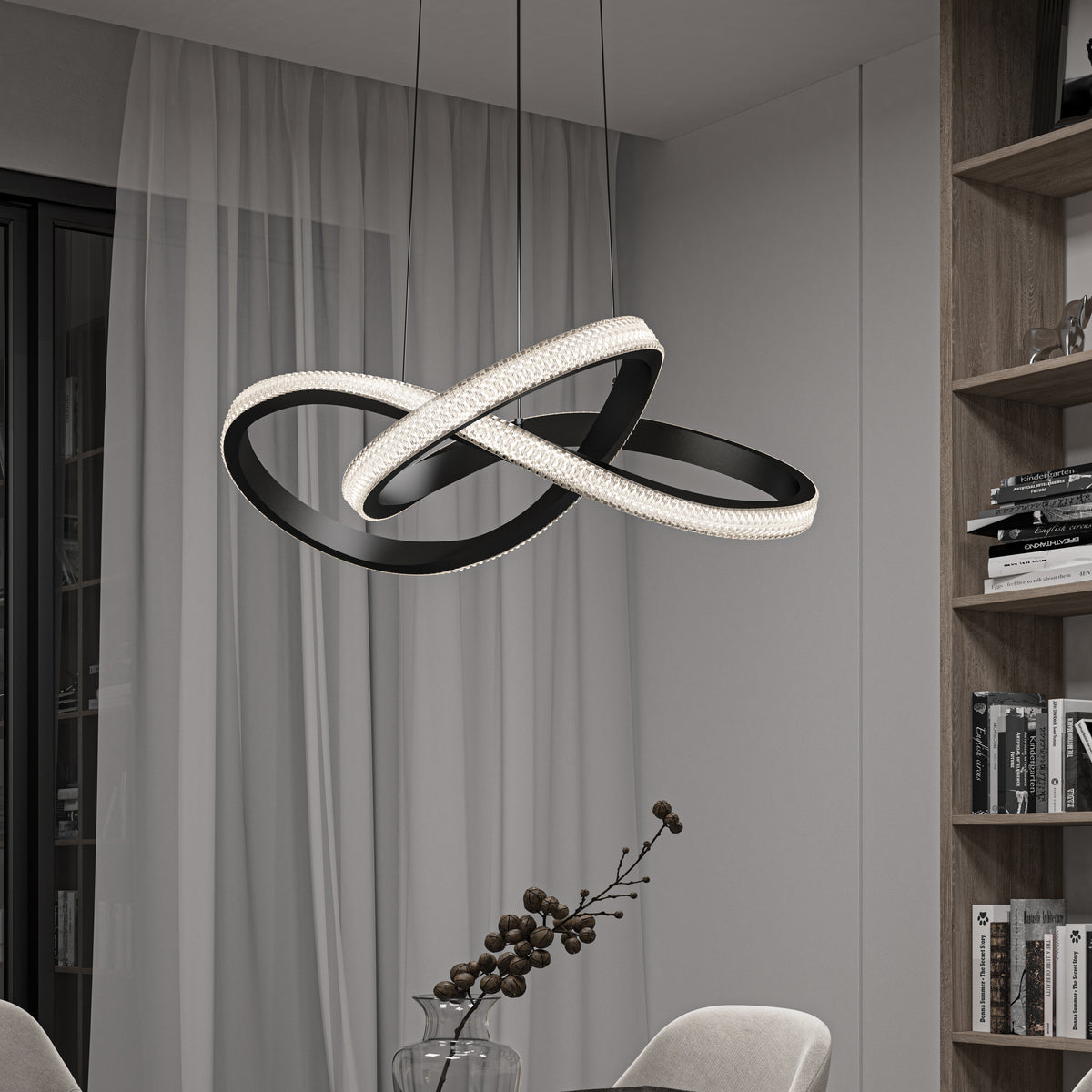 A modern dining room features a sculptural black LED chandelier with intertwined loops, hanging above a table with a glass vase and decorative branches. Sheer curtains and shelves with books are visible in the background.