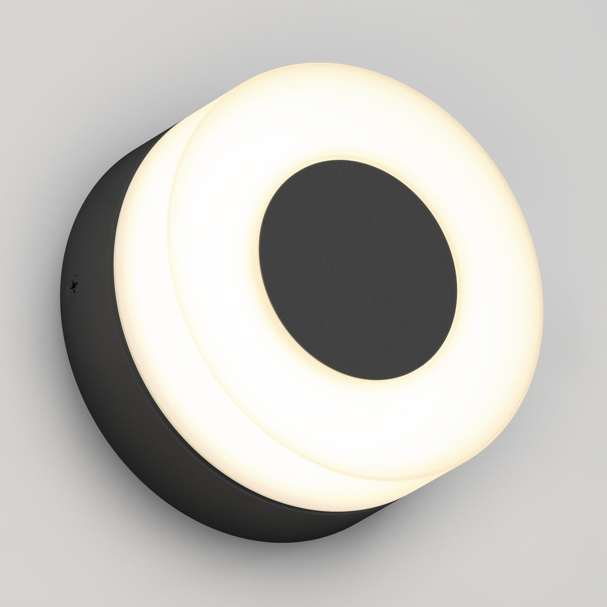 The Artika Ludwig modern LED indoor-outdoor wall light 5CCT features a round black central circle and outer ring, emitting a soft, even white glow, and is shown mounted on a light gray wall.