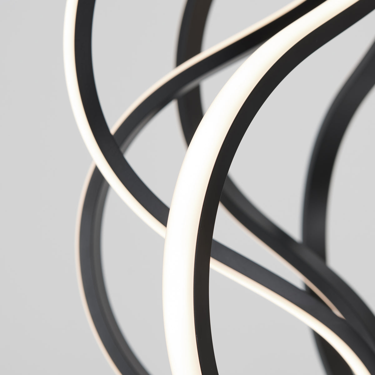 Close-up of intertwined, curved black and white LED light strips against a plain, light gray background. The design is abstract and modern, with smooth lines and a glowing effect.