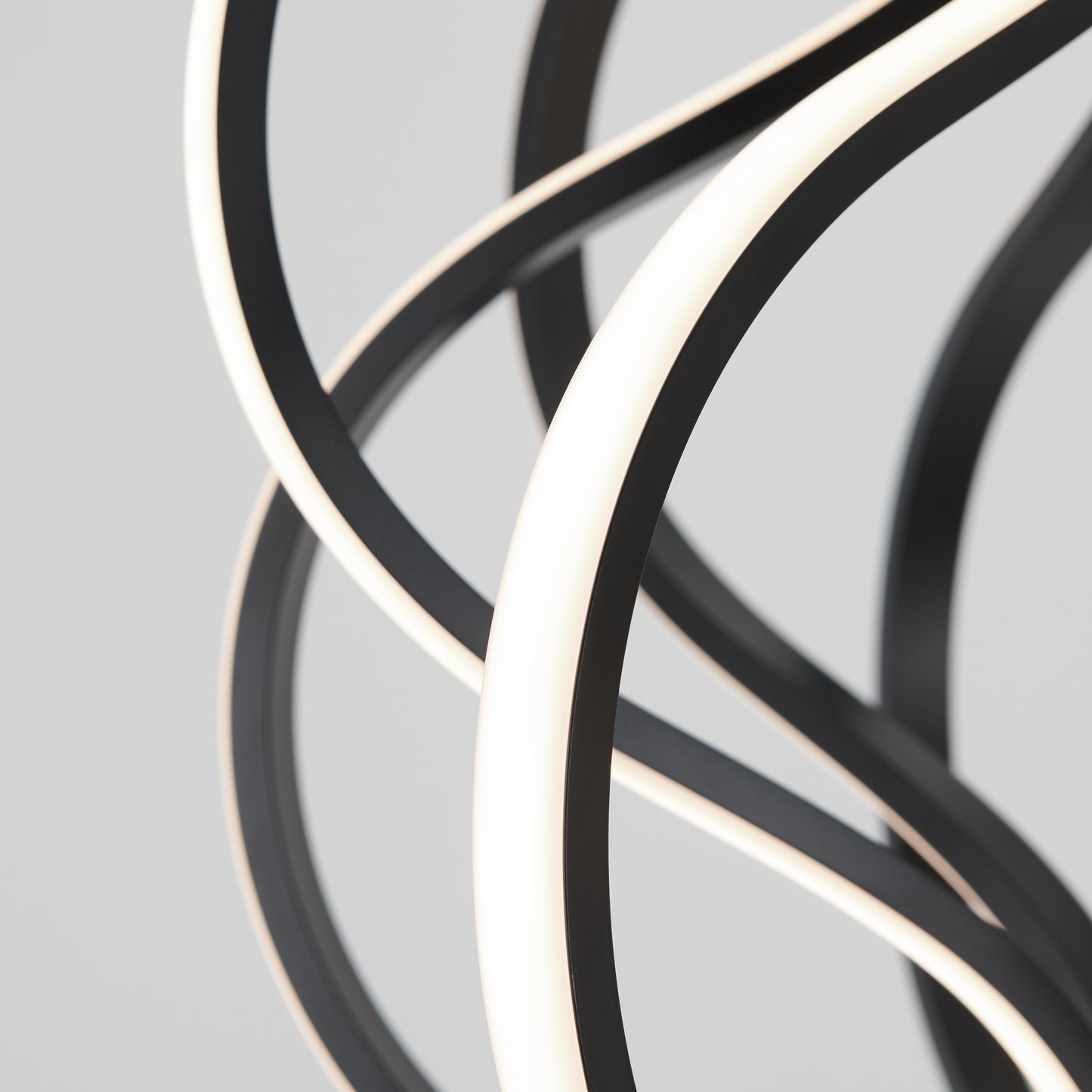 Close-up of intertwined, curved black and white Meridian LED pendant lights by Artika set against a plain light gray background, creating an abstract and modern design.