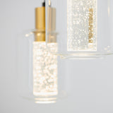 Close-up of two modern pendant lights with cylindrical glass covers and gold accents, featuring sparkling bubbles inside illuminated glass rods, against a light background.