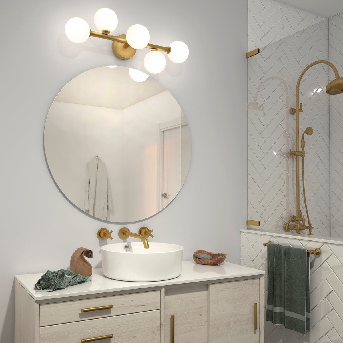 Modern bathroom with a round mirror above a white vanity, gold faucet and fixtures, vessel sink, globe light, green towels, the Artika Bloom 27-in 3-Light Modern LED Vanity Light for elegant lighting, and a glass shower with gold accents and herringbone tiles.