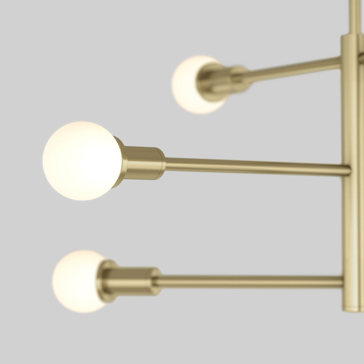 Close-up of a modern brass light fixture with three horizontal arms, each holding a glowing round bulb, against a plain light gray background.