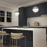 Modern kitchen with navy cabinets, white countertops, island seating with beige chairs, white subway tile backsplash, cutting boards, and two spherical pendant lights hanging above the island.