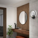 A modern entryway features a wooden console table with decor, a round mirror on a wooden slat wall, a small plant, an orange bench, and a circular wall sconce with soft lighting.