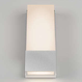 The Artika Dixon indoor-outdoor LED wall light features a brushed metal base and a rectangular frosted glass shade, casting soft, warm light against a light gray background.