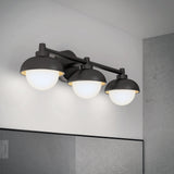A modern three-light vanity fixture with matte black metal shades and frosted glass globes, mounted above a bathroom mirror on a light gray wall.