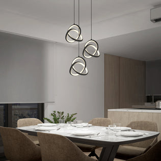 A modern dining room features a marble table for four, brown upholstered chairs, neutral walls, a large window, minimal decor with a plant centerpiece, and the Artika Zephyr 3-light LED pendant illuminating the space above.