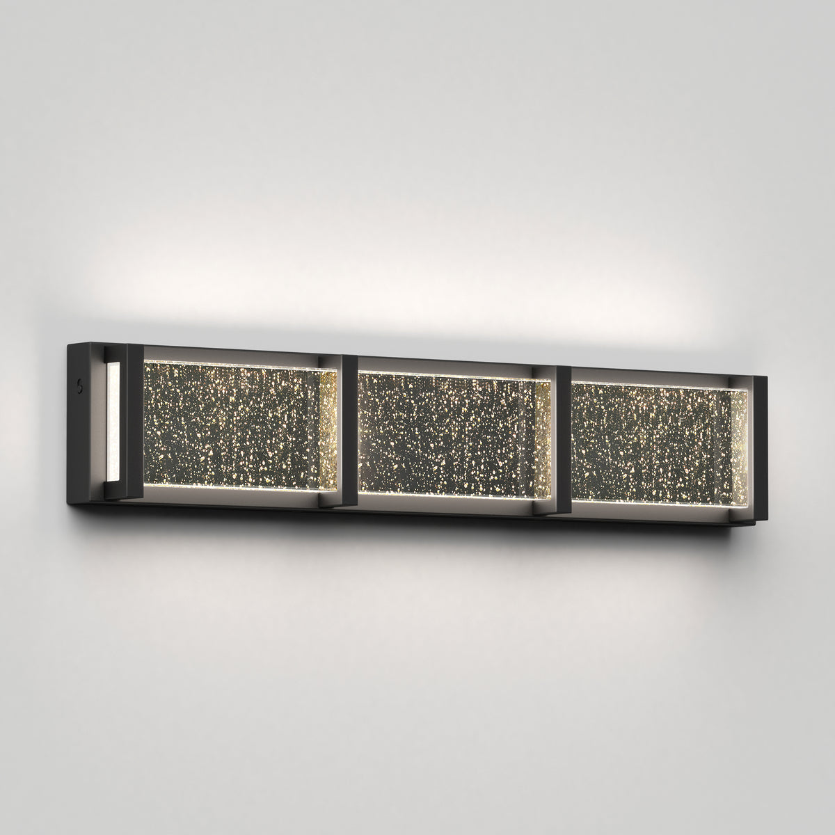 A modern rectangular wall sconce with three illuminated glass panels featuring bubble-like patterns, mounted on a light gray wall.