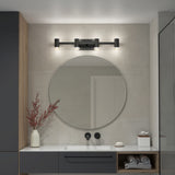 Modern bathroom with a round mirror above a white sink, black wall-mounted faucet, and a black four-light fixture. A vase with red branches, soap dish, and neatly rolled towels decorate the countertop and shelf.