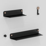 Two black metal wall shelves with wooden accents and two matching hooks are mounted on a white wall, creating a minimalist and modern storage display.