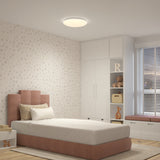 A cozy bedroom with a single bed, soft pink headboard, polka dot wallpaper, white built-in cabinets, toys, a window seat with cushions, and a round ceiling light.