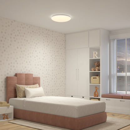 A modern, cozy bedroom with a single bed, soft pink and beige decor, built-in white storage, window seat, plush toys on shelves, patterned wallpaper, and an Artika Empress 13 in. LED modern flush mount ceiling light.