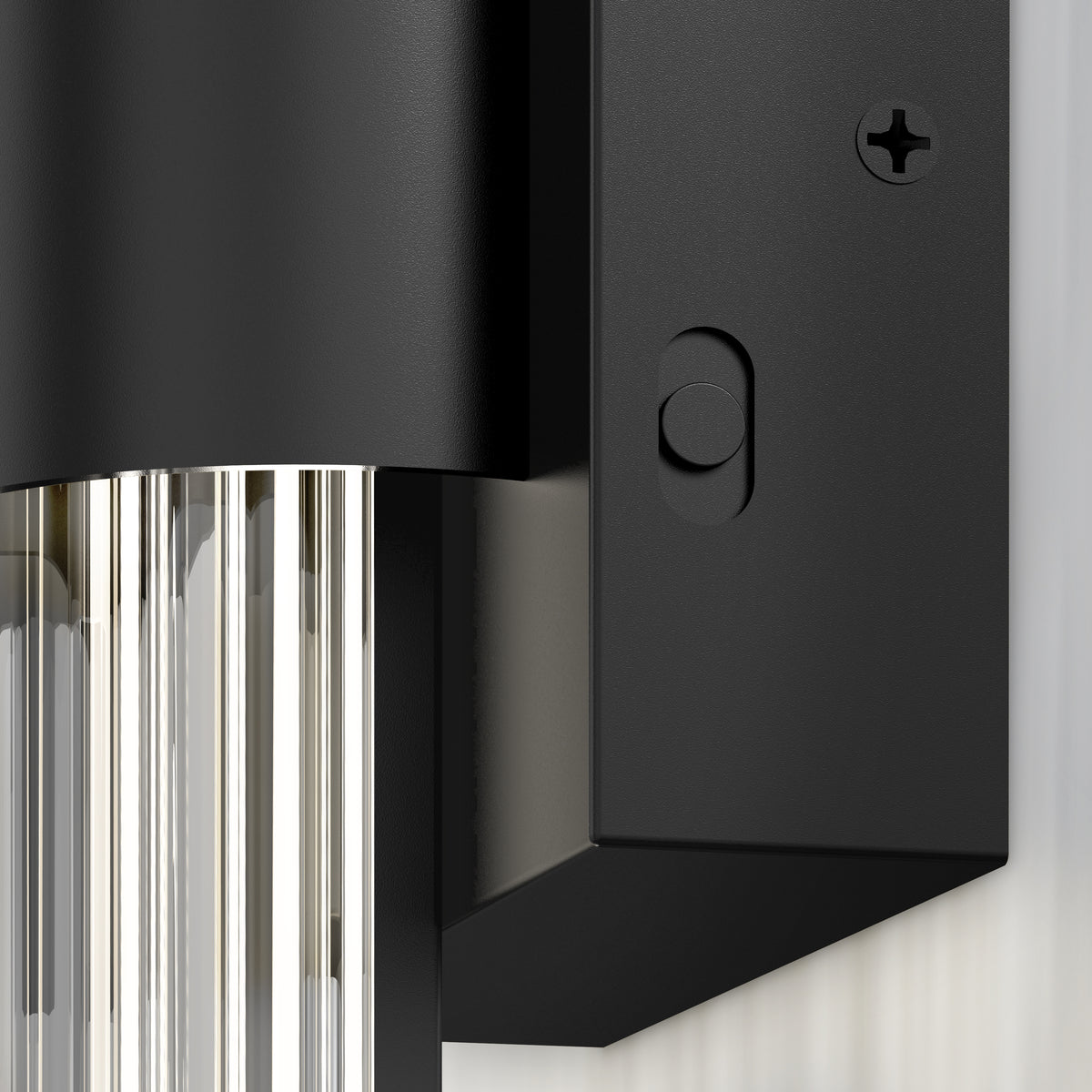 Close-up of the Artika Dorado contemporary LED wall sconce 3 CCT, featuring a black and gold finish, rectangular base with visible screw, and vertically ridged cylindrical glass shade, mounted on a light-colored wall.