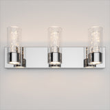 A modern wall-mounted light fixture with three cylindrical glass shades, each containing small sparkling lights, set on a shiny rectangular chrome base against a beige wall.
