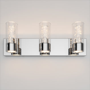 Artika Essence 3 LED bathroom vanity light with cylindrical glass shades and sleek chrome finish on a light wall.