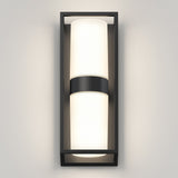 A modern wall sconce with a rectangular black frame and a central cylindrical frosted glass light diffuser, glowing warmly against a light gray wall.