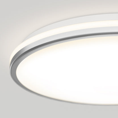 A close-up of the Artika Macy 15 in. LED modern flush mount light, featuring a white and silver frame, emits a soft, diffused glow. This RGB WiFi-enabled ceiling fixture stands out against a light gray background.