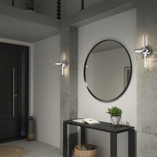 Modern entryway with a round wall mirror above a black console table, decorated with a potted plant and books. Concrete walls feature two Artika Swirl LED Sconces, and a basket sits below the table.