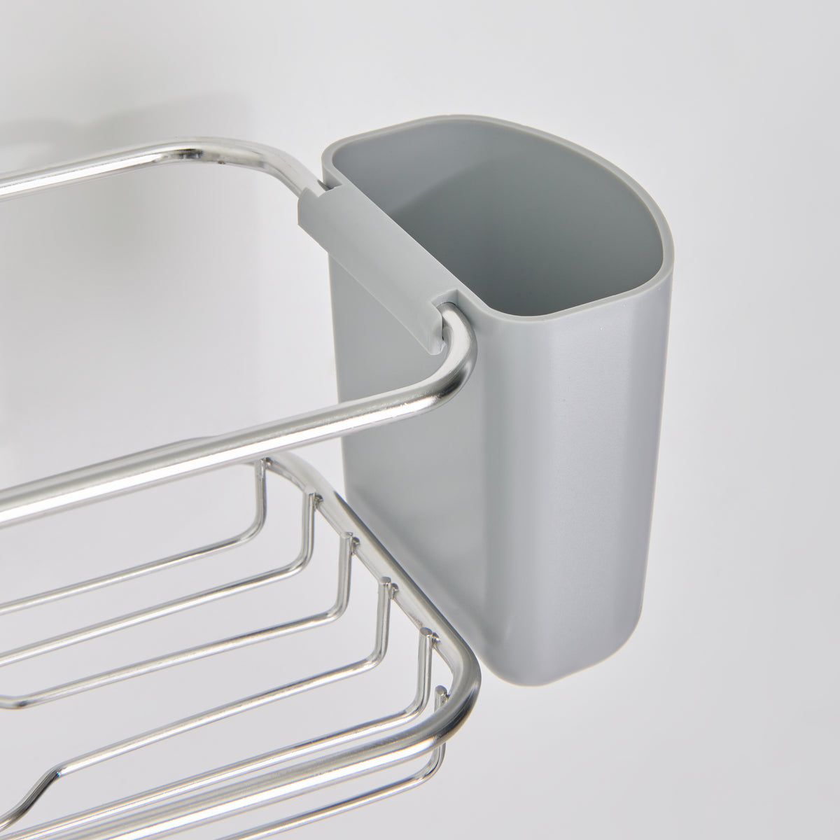 A close-up of a gray plastic container attached to a metal rack, which is mounted on a white wall. The container is open at the top and has a rounded rectangular shape.
