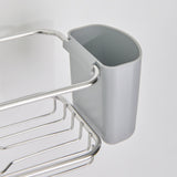 A close-up of a gray plastic container attached to a metal rack, which is mounted on a white wall. The container is open at the top and has a rounded rectangular shape.