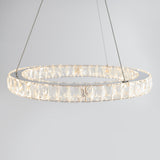 A modern circular chandelier with clear crystal accents, suspended by thin wires against a plain light gray background. The chandelier emits a soft, warm light.