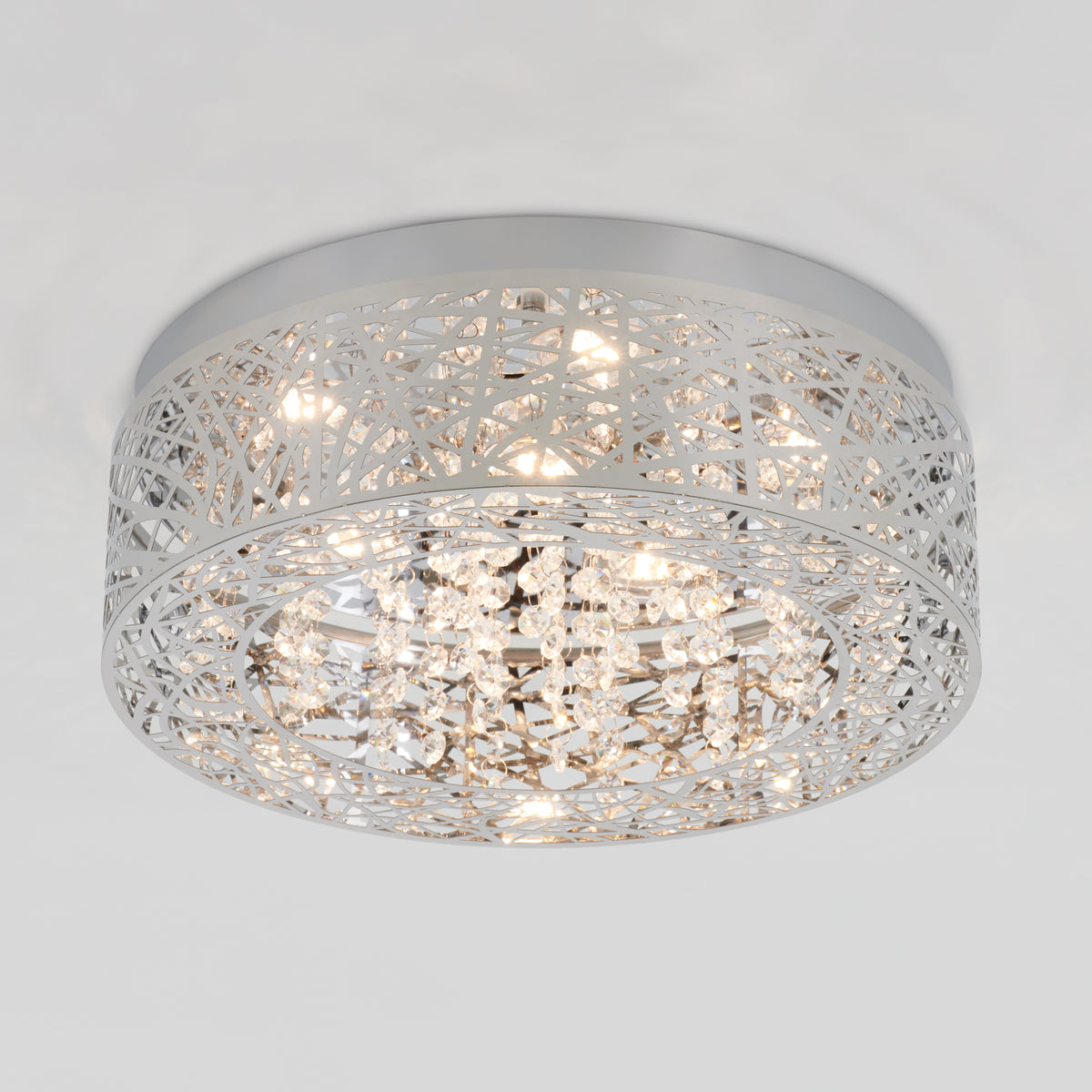 A modern ceiling light fixture with a round, silver metal frame featuring an intricate cutout pattern and hanging crystal accents, illuminated against a plain white ceiling.