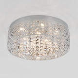 A modern ceiling light fixture with a round, silver metal frame featuring an intricate cutout pattern and hanging crystal accents, illuminated against a plain white ceiling.