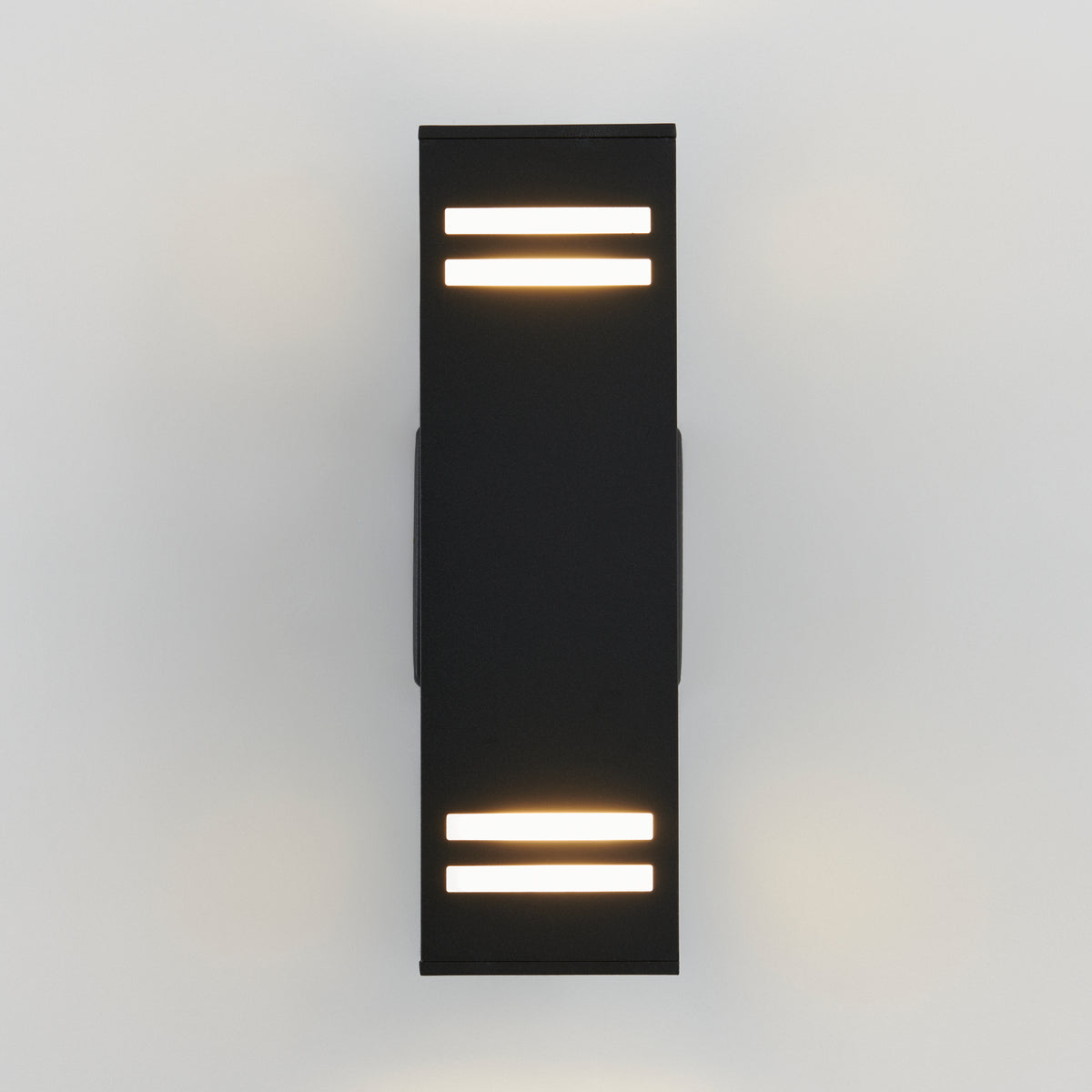 A modern, rectangular black wall sconce with two horizontal light strips at both the top and bottom, mounted on a white wall and emitting a soft glow.