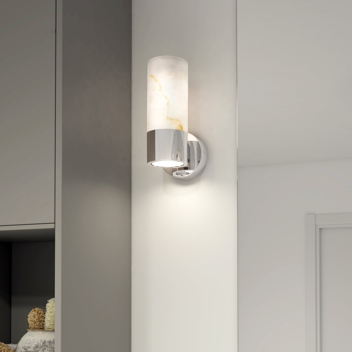 A modern wall sconce with a cylindrical marble shade and chrome base is mounted on a white wall in a contemporary interior setting.