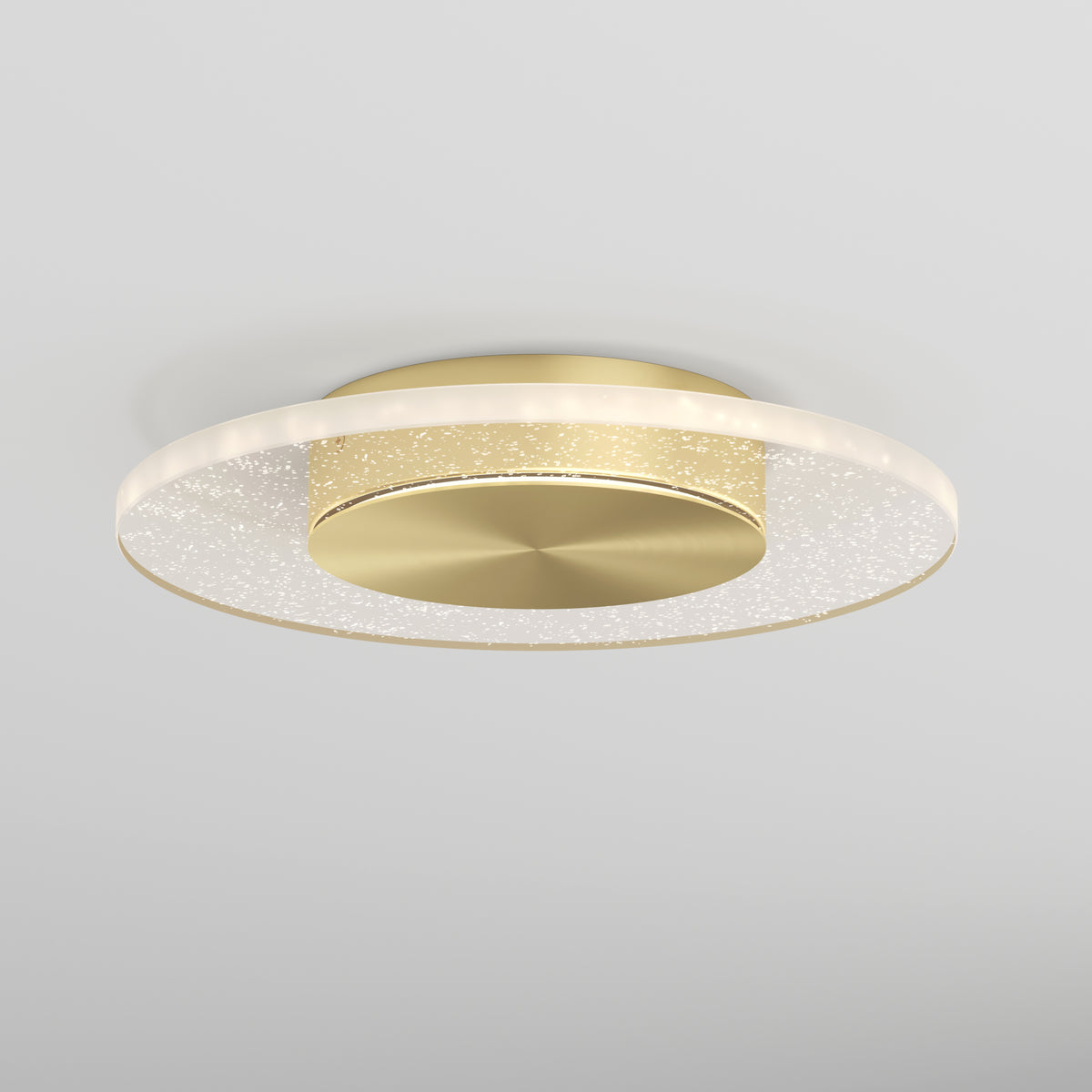 The Artika Essence Disk LED flush mount is a modern ceiling light with a circular gold base and a clear, ring-shaped rim with subtle sparkles, designed for white ceilings.