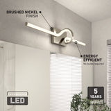 Modern LED wall light with a brushed nickel finish is mounted above a bathroom mirror. Text highlights its energy efficiency, integrated LED feature, and a 5-year warranty. A window with blinds and a plant are nearby.