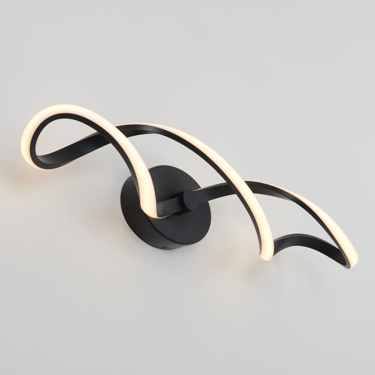 A modern wall sconce with two intertwined, curved LED light strips mounted on a round black base against a plain white wall.