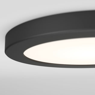 Close-up of the Artika Europa Disk 7 in. LED modern flush mount light, featuring a round black design with a frosted white cover, mounted on a white ceiling and illuminated.