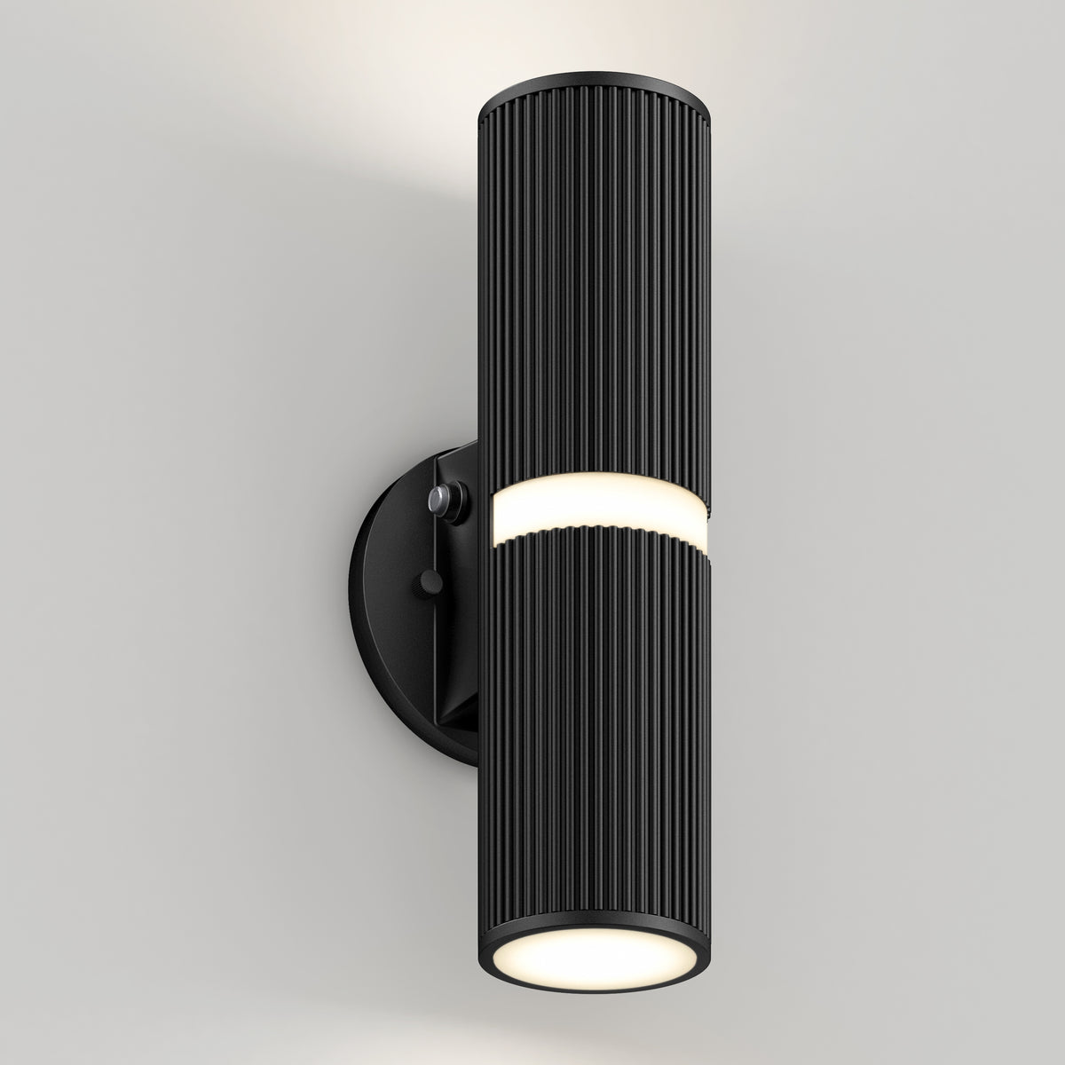 The Artika Groove LED indoor-outdoor wall light features a modern black cylindrical design with vertical ridges, emitting light from the top, bottom, and center band, and mounts on a round black base against a light wall.