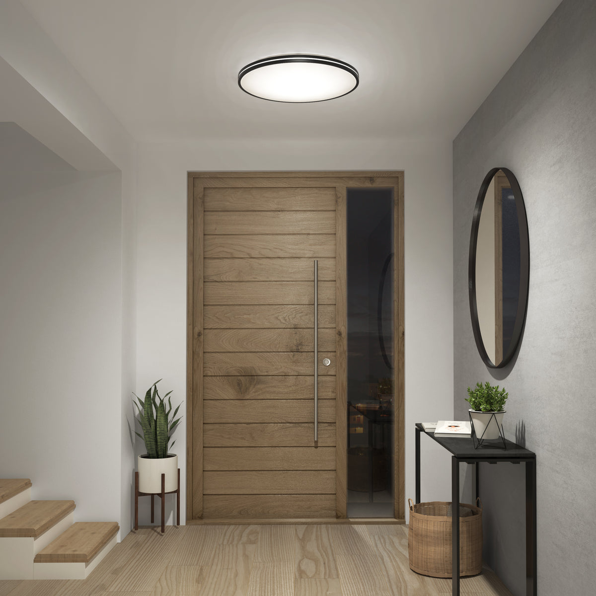 A modern entryway with a wooden front door, a round ceiling light, a small console table with décor items, a potted plant, a round wall mirror, and a basket on a light wood floor next to a staircase.
