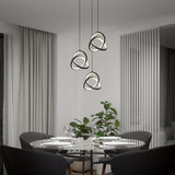 A modern dining room with a glass table set for four, surrounded by gray chairs, a potted plant, large windows with drapes, and three sculptural pendant lights hanging above the table.