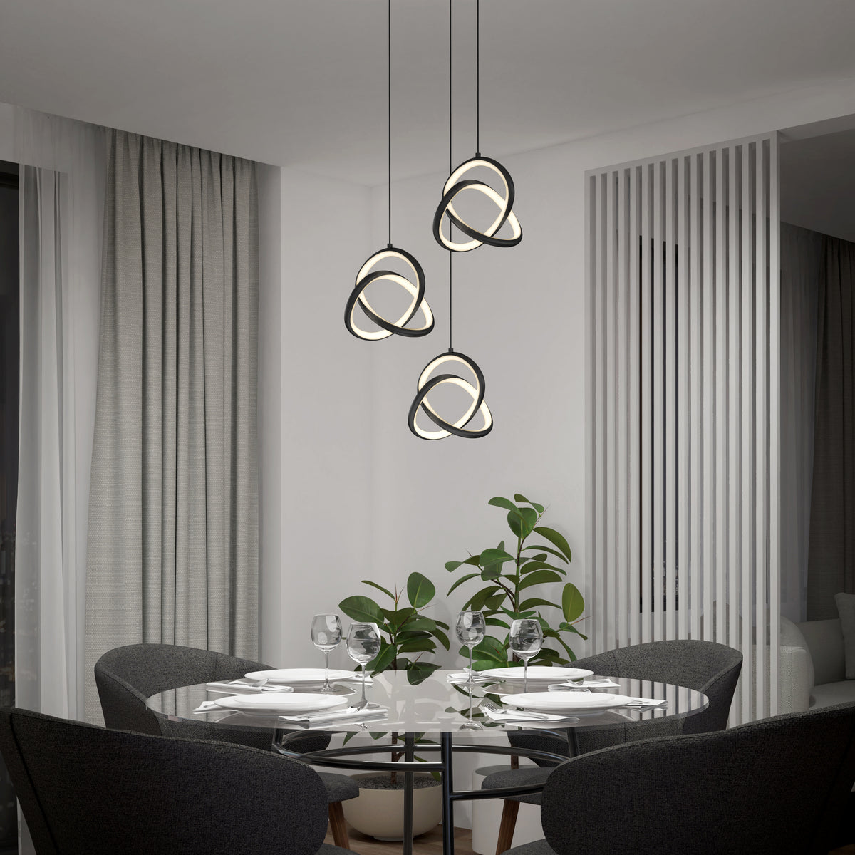 A modern dining room features a glass round table for four, gray chairs, and the Artika Zephyr 3-light LED pendant above. A leafy plant sits nearby, next to large curtains and vertical white panel dividers.