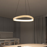 A modern, circular pendant light with a wooden finish hangs above a dining table in a contemporary kitchen and dining area with neutral tones, minimalist furniture, and sheer curtains.