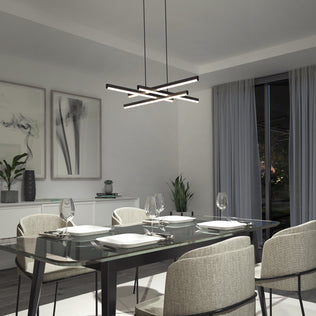 A modern dining room features a glass table for four, beige upholstered chairs, abstract wall art, indoor plants, and the Artika Grid LED pendant light. Large windows with sheer curtains provide a nighttime view outside.