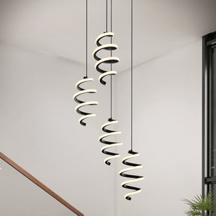 The Artika Chorus 4 Light LED Pendant (5 CCT) hangs from the ceiling in a bright, minimal room with white walls, a staircase railing, and a plant visible in the lower right corner.