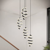 Three modern spiral pendant lights with glowing LED strips hang from the ceiling in a minimalistic interior, next to a staircase and a large window. A green plant is partly visible in the lower right corner.