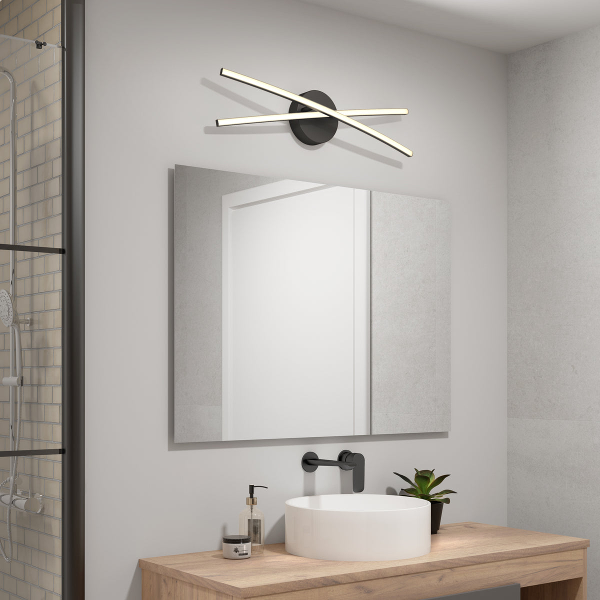 A modern bathroom with a rectangular mirror, a white sink on a wooden counter, a black faucet, a small potted plant, and a contemporary wall light fixture above the mirror with two intersecting LED bars.