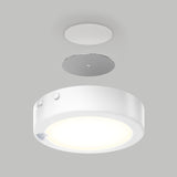 A modern round ceiling light fixture with a white casing, shown below a matching mounting plate and cover, all set against a plain light gray background. The fixture is illuminated, emitting a soft glow.